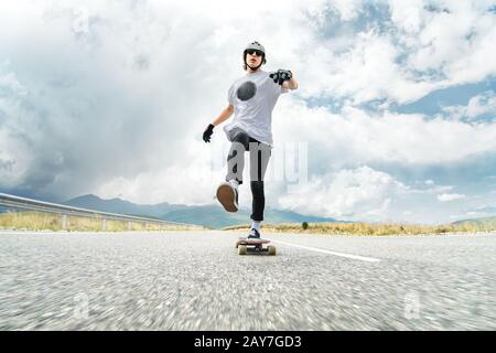 Ein Mann in einem Helm und einer Sonnenbrille beschleunigt das Drücken seines Fußes auf sein Longboard Stockfoto