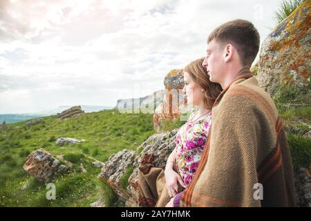 Porträt eines Kerls mit einem Mädchen, das in einer Decke bedeckt ist, die in einer Umarmung in der Natur steht und mit Glück lächelt Stockfoto