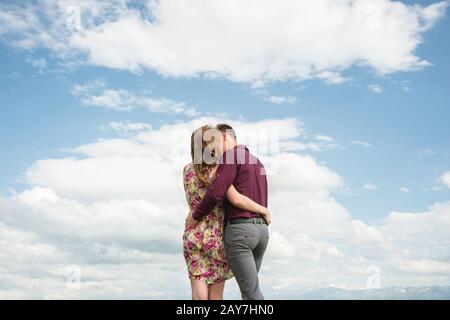 Ansicht von hinten. Junges Paar umarmte Küsse gegen den blauen Himmel und weiße Wolken. Stockfoto