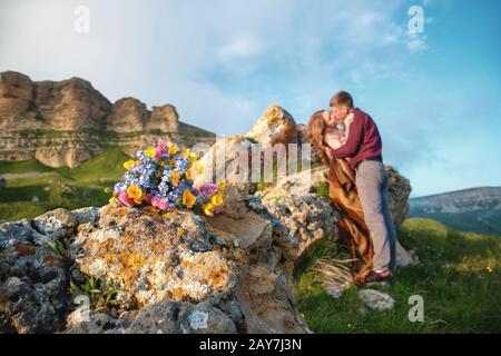 Ein Hochzeitsbouquet im rustikalen Stil vor dem Hintergrund verschwommener junger Jungvermählter an einem schönen natürlichen Ort bei Sonnenuntergang Stockfoto
