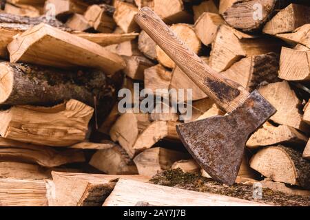 Die Axt steckt vor dem Hintergrund von gehacktem Brennholz, das in einem flachen Haufen liegt, in einem Holzholz Stockfoto
