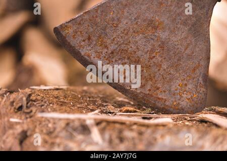 Die Klinge der Axt steckt in einem Holzstich vor dem Hintergrund von gehacktem Brennholz, das in einem flachen Haufen liegt. Stockfoto