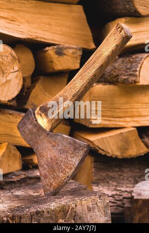 Die Axt steckt vor dem Hintergrund von gehacktem Brennholz, das in einem flachen Haufen liegt, in einem Holzholz Stockfoto