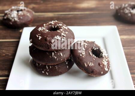 Hausgemachte Schokoladendonnuts. Passt die Packungen an. Amerikanische Donuts mit einem Loch. Hausgemachte Süßigkeiten Schokoladenpakete mit Kokosnuss. Stockfoto