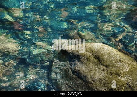 Kleine bunte Steine am Ufer eines Gebirgsstroms mit kristallklarem Gletscherwasser. Draufsicht. Stockfoto