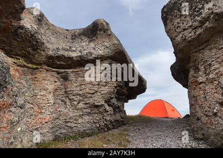 Ein orangefarbenes Zelt steht hoch in den Bergen zwischen zwei hohen Felsen Stockfoto