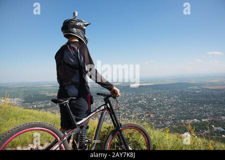 Ein junger Kerl, der auf Ihrem Mountainbike-Rad auf einem Berg steht, wenn er unter den Bergen tief Wolken zeigt Stockfoto