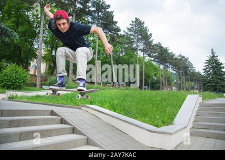 Langhaariger Skater-Teenager in einem T-Shirt und einem Sneaker-Hut springt eine Gasse gegen einen stürmischen Himmel Stockfoto