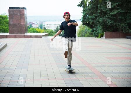 Ein Kerl in einer Kappe beschleunigt, indem er seinen Fuß auf sein Skateboard drückt Stockfoto