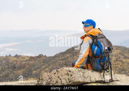 Ein einsamer Tourist mit Rucksack und Sonnenbrille ruht auf einem Felsen Stockfoto