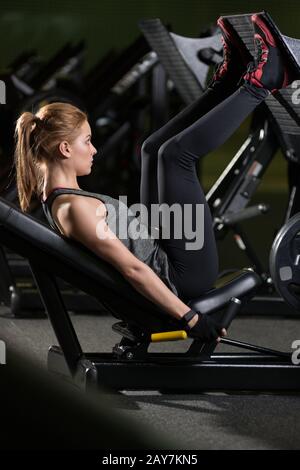 Sportliche Frau mit Gewichten-Presse-Maschine für die Beine. Fitness-Studio. Stockfoto