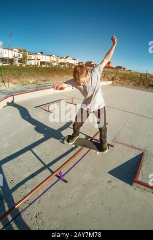 Teenager Skater in einem Hoodie Sweatshirt und Jeans gleiten über einem Geländer auf einem Skateboard in einem Skatepark Stockfoto