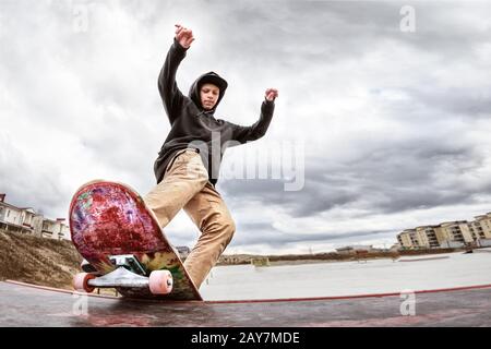 Teenager Skater in einem Hoodie Sweatshirt und Jeans gleiten über einem Geländer auf einem Skateboard in einem Skatepark Stockfoto