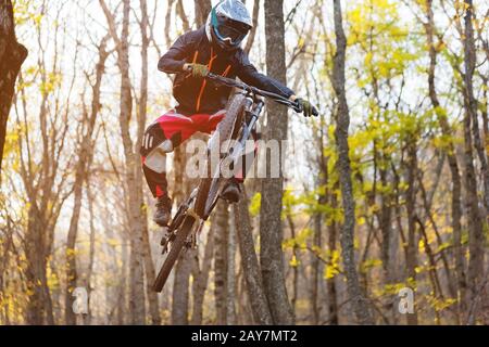 Ein junger Fahrer am Rad seines Mountainbikes macht einen Trick beim Springen auf dem Sprungbrett des bergab Bergweges im Stockfoto