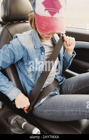 Ein Hüftmädchen, das Jeanskleidung trägt, befestigt ihren Sicherheitsgurt im Auto. Stockfoto