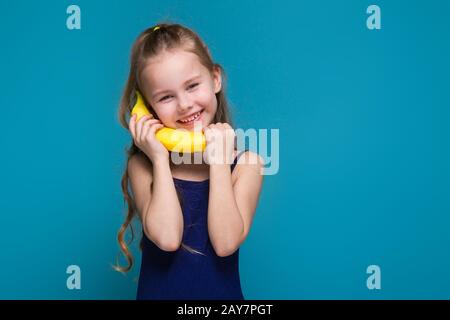 Hübsches, kleines Mädchen im Hemd mit brunet-haaren hält eine Banane Stockfoto