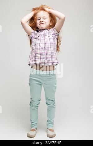 Süßes Mädchen mit Rotkopf in Plaid Hemd, leuchtend blaue Hose und weiße Stiefel Stockfoto