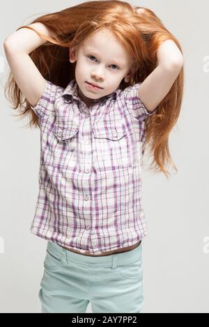 Sehr süßes Mädchen mit Rotkopf in Plaid Hemd, leuchtend blaue Hose und weißen Stiefeln Stockfoto