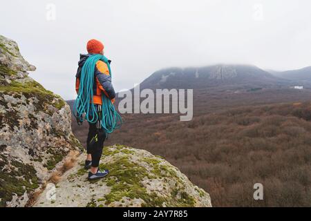 Professioneller Bergsteiger mit einer Seilbucht steht auf einem hohen Felsen und blickt in die Ferne Stockfoto