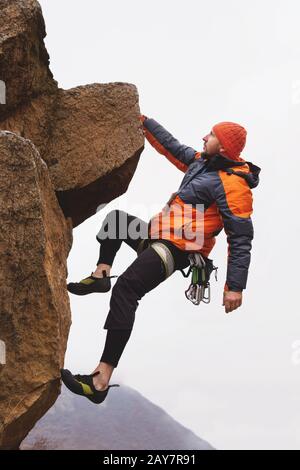 Hiphster - Kletterer hängend auf einer Hand auf einem Felsen vor dem Hintergrund der kaukasischen Berge im späten Herbst. Stockfoto