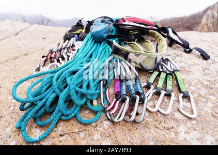 Kletterausrüstung - Seil- und Carbinenblick von der Seitennaht. Ein auf dem Boden liegendes gewickeltes Kletterseil als Hintergrund. Stockfoto