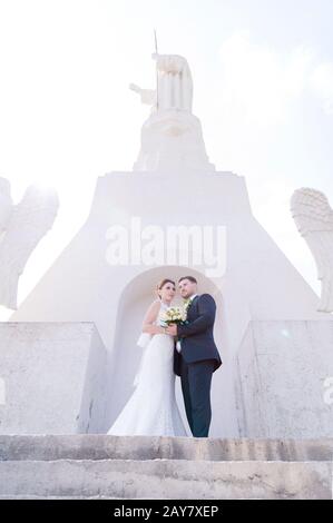 Porträt eines schönen Paares, das an einem Hochzeitstag mit einem Blumenstrauß in der Hand vor dem Hintergrund eines orthodoxen Christen gegraben wurde Stockfoto