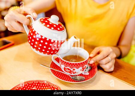 Ein Mädchen in einem Café gießt Tee aus einer Teekanne in einen Becher. Stockfoto