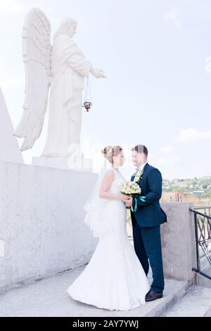 Porträt eines schönen Paares, das an einem Hochzeitstag mit einem Blumenstrauß in der Hand vor dem Hintergrund eines orthodoxen Christen gegraben wurde Stockfoto