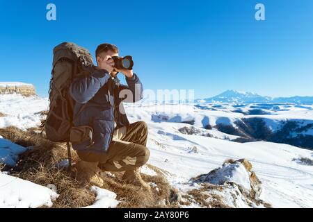 Das Porträt eines bärtigen Hüpflings, eines Fotografen mit Rucksack und Sonnenbrille macht Fotos von seiner DSLR Stockfoto