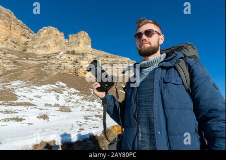 Portrait EIN bärtiger Hippie-Fotograf mit Rucksack und Sonnenbrille mit großem Rucksack auf seinen Schultern steht mit Witz Stockfoto