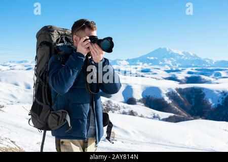 Das Porträt eines bärtigen Hüpflings, eines Fotografen mit Rucksack und Sonnenbrille macht Fotos von seiner DSLR Stockfoto