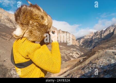 Eine Fotografin im Fellhut und ein gelber Pullover in den Bergen fotografiert auf ihrer Digitalkamera. Stockfoto