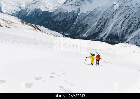 Zwei Ski-Freerider klettern mit der Ausrüstung auf dem Rücken, die am Rucksack befestigt ist, in tiefes Schneepulver. Stockfoto