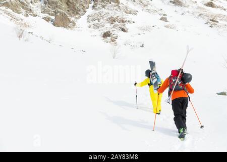 Zwei Ski-Freerider klettern mit der Ausrüstung auf dem Rücken, die am Rucksack befestigt ist, in tiefes Schneepulver. Stockfoto