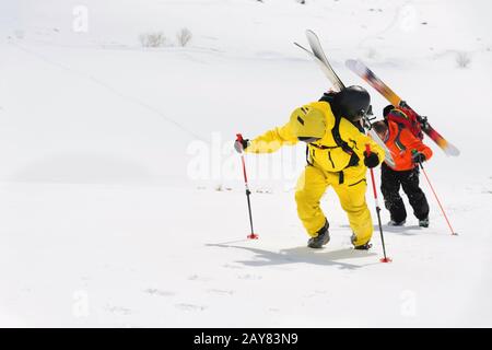 Zwei Ski-Freerider klettern mit der Ausrüstung auf dem Rücken, die am Rucksack befestigt ist, in tiefes Schneepulver. Stockfoto