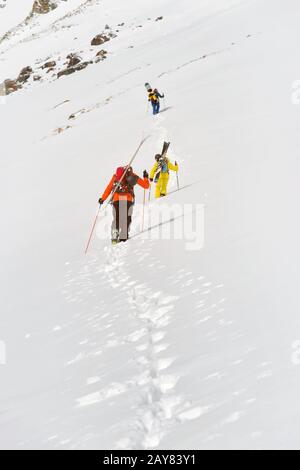 Zwei Ski-Freerider klettern mit der Ausrüstung auf dem Rücken, die am Rucksack befestigt ist, in tiefes Schneepulver. Stockfoto