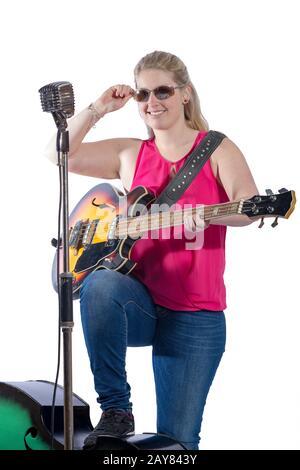 Junge Frau in rotem T-Shirt und Jeans, die vor einem Mikrofon mit E-Gitarre steht Stockfoto