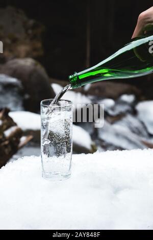 Mineralwasser wird aus einer gläsernen grünen Flasche in einen durchsichtigen Glasbecher gegossen. Stockfoto