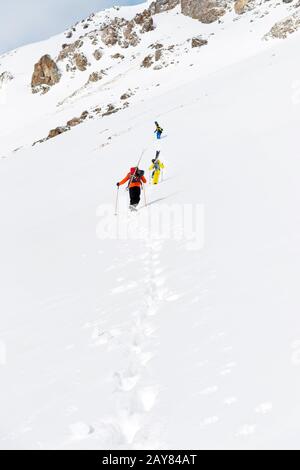 Zwei Ski-Freerider klettern mit der Ausrüstung auf dem Rücken, die am Rucksack befestigt ist, in tiefes Schneepulver. Stockfoto