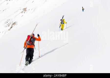 Zwei Ski-Freerider klettern mit der Ausrüstung auf dem Rücken, die am Rucksack befestigt ist, in tiefes Schneepulver. Stockfoto