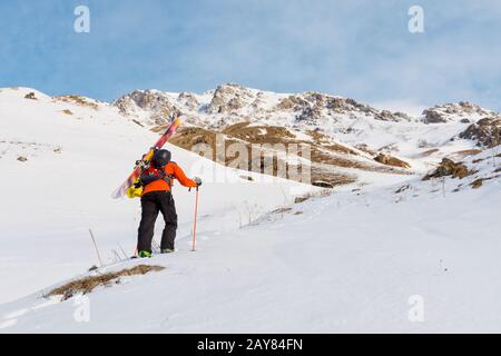 Der Skifahrer steigt mit der Ausrüstung auf dem Rücken, die am Rucksack befestigt ist, in tiefes Schneepulver. Stockfoto