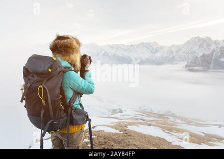 Das Porträt eines süßen Touristenmädchens in einem großen Fellhut fotografiert auf ihrer Digitalkamera in den Bergen. Stockfoto