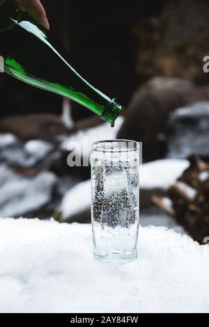 Reines Mineralwasser wird bis zum letzten Tropfen aus einer glasgrünen Flasche in einen durchsichtigen Glasbecher gegossen. Stockfoto