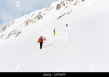 Zwei Ski-Freerider klettern mit der Ausrüstung auf dem Rücken, die am Rucksack befestigt ist, in tiefes Schneepulver. Stockfoto