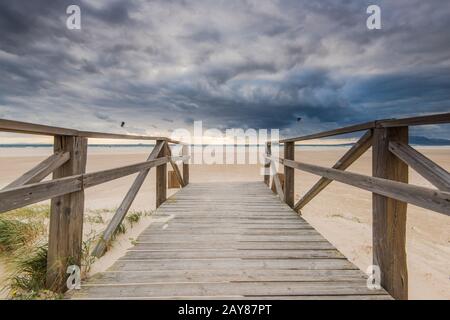 holzbrücke am Strand mit dunklen Wolken vor Sturm Stockfoto