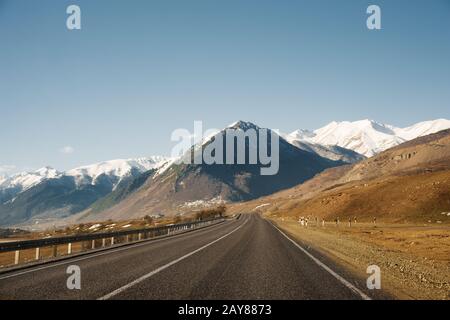 Blick auf die Herbststraße, die zu den Bergen zu den schneebedeckten Gipfeln des Kaukasus führt. Das Konzept, zur Halterung zu fahren Stockfoto