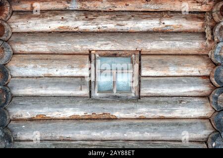 Die Wand eines alten Holzhauses aus Holzstämmen mit Fenster. Stockfoto