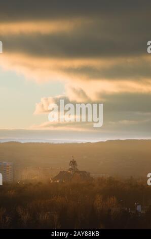 Stadtherbstlandschaft des Parkteils der Stadt im Vorrauchhals in warmen Tönen. Katholische Kirche vor dem Hintergrund o Stockfoto