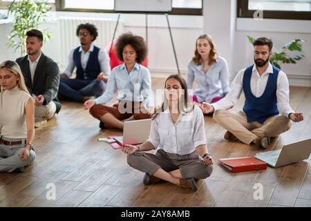 Eine Gruppe von Mitarbeitern, die bei der Arbeit meditieren und auf dem Boden sitzen. Modern, Business, Meditation Stockfoto