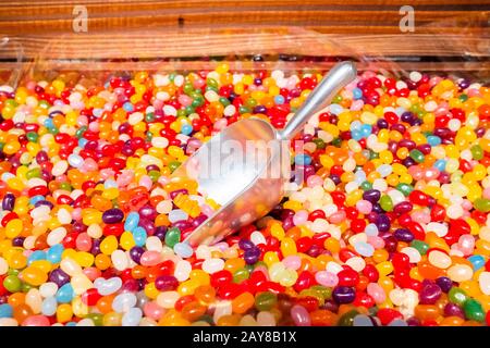 Aluminiumschaufel in einer Streuung von runden hellen mehrfarbigen Marmalade Gelee Bohnen auf einem Ladentisch. Leckere und gesunde Fruchtsaftbehandlung Stockfoto